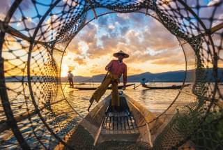 Fisherman in Inle Lake framed by basket sunset Myanmar